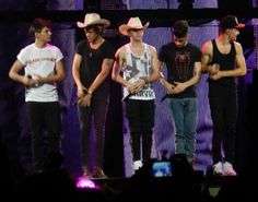 the one direction band is performing on stage with their hands in their pockets and wearing cowboy hats