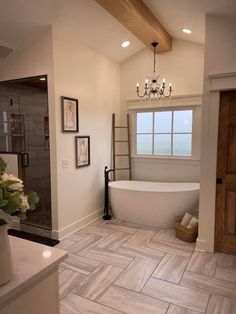 a large white bath tub sitting in a bathroom next to a sink and window with a chandelier above it