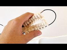 a hand holding a piece of white yarn over a string with the end of it being crocheted