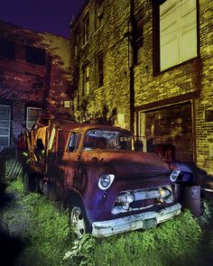 an old truck parked in front of a brick building at night with the headlights on