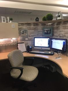 an office cubicle with two computer screens on the wall and a chair in front of it