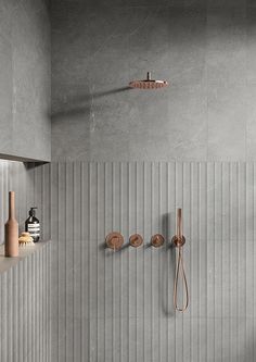 a bathroom with grey tiles and wooden fixtures on the wall, along with copper shower faucets