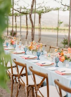 a long table set with blue and orange plates, napkins and flowers in vases