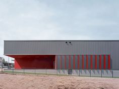 an industrial building with red and grey stripes on the side, next to a dirt field