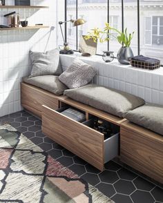 a window seat with storage underneath it in front of a large window, next to a rug and potted plants