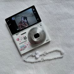 a cell phone sitting on top of a white bed next to a beaded necklace