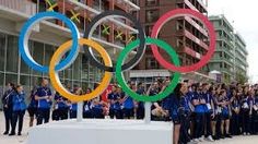 a group of people standing next to each other in front of a large sign with the olympic rings on it