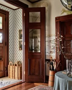 an entry way with wooden doors and baskets on the table next to it, in front of a wallpapered wall