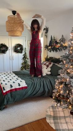 a woman standing on top of a bed next to a christmas tree in a bedroom