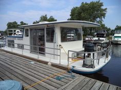 a houseboat docked at a dock with other boats in the water and trees behind it