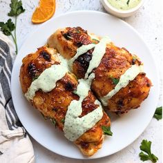 three pieces of chicken covered in sauce on a white plate next to an orange slice