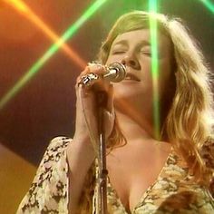 a woman singing into a microphone while standing in front of a green and yellow light