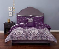 a bed with purple and white comforters in a room next to a wall mounted clock