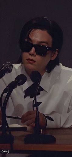 a man wearing sunglasses sitting at a table with microphones in front of his face