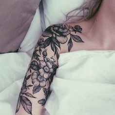 a woman laying in bed with a tattoo on her arm