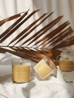 two candles sitting on top of a bed next to a palm leaf and a glass jar