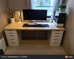 a desk with a computer monitor, keyboard and plant on it in front of a window