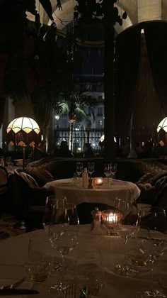 a dimly lit dining room with wine glasses on the table and candles in the middle