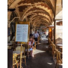 people are sitting at tables and chairs under an arched ceilinged area with signs on the walls