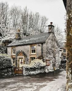 an old stone house surrounded by trees and bushes in the wintertime with snow on the ground