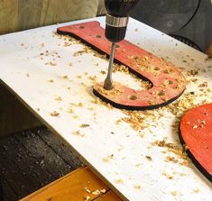 a drill is being used to make letters with wood shavings on a table