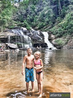 two young children standing in the water near a waterfall with people swimming and playing around