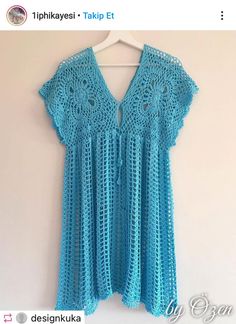 a blue crocheted top hanging on a white wall next to a hanger