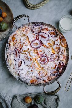 a cake covered in powdered sugar sitting on top of a table next to fruit