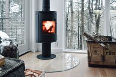 a wood burning stove in a living room next to a window with lots of trees outside