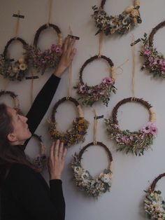 a woman is arranging wreaths on the wall with flowers hanging from it's sides