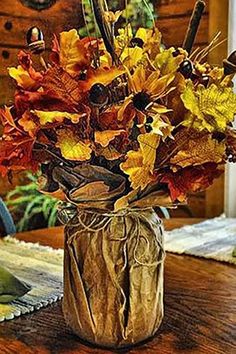 a vase filled with lots of colorful leaves on top of a wooden table next to a clock