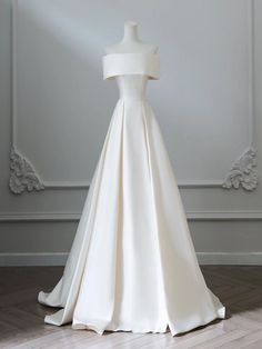 a white wedding dress on display in front of a wall with an ornate frame behind it