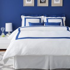 a bedroom with blue walls and white bedding, two framed pictures on the wall