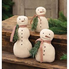 three snowmen sitting next to each other on top of a wooden box filled with pine branches