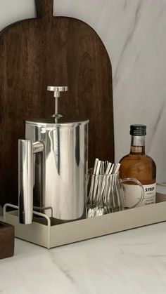 a wooden cutting board sitting on top of a counter next to a metal container filled with drinks