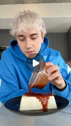 a boy in a blue hoodie is pouring caramel sauce on a piece of cake