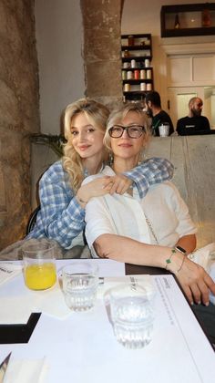 two women sitting next to each other at a table with drinks in front of them