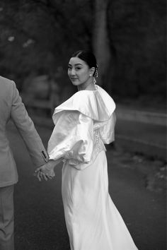 a man and woman are holding hands while walking down the street in black and white