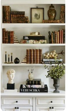 a white book shelf filled with books and vases on top of it's shelves