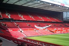 an empty soccer stadium with red seats and green grass on the sidelines is seen in this image