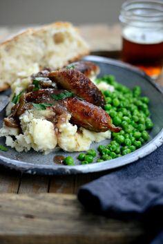 a plate filled with meat, mashed potatoes and peas next to a glass of beer