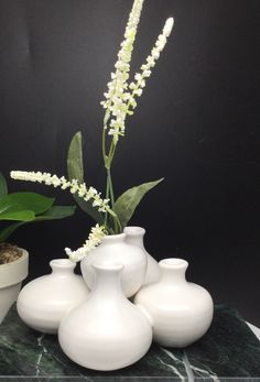 four white vases with flowers in them on a green marble table next to a potted plant