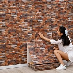 a woman kneeling on the floor next to a wall with bricks covering it and reaching out for something