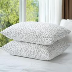 two pillows stacked on top of each other on a bed in front of a window