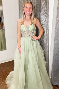 a woman in a green dress standing next to a wall with silver sequins on it