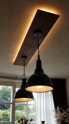 two lights hanging from the ceiling above a dining room table with flowers in vases