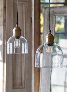 two clear glass pendant lights hanging from a wooden ceiling in front of a door and window