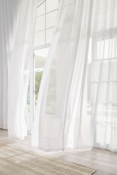 a white room with sheer curtains and a rug on the floor in front of a sliding glass door