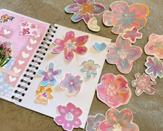 an open notebook with paper flowers and hearts on the pages, next to a bunch of stickers