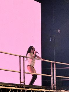 a woman standing on top of a metal rail next to a pink wall and holding a microphone